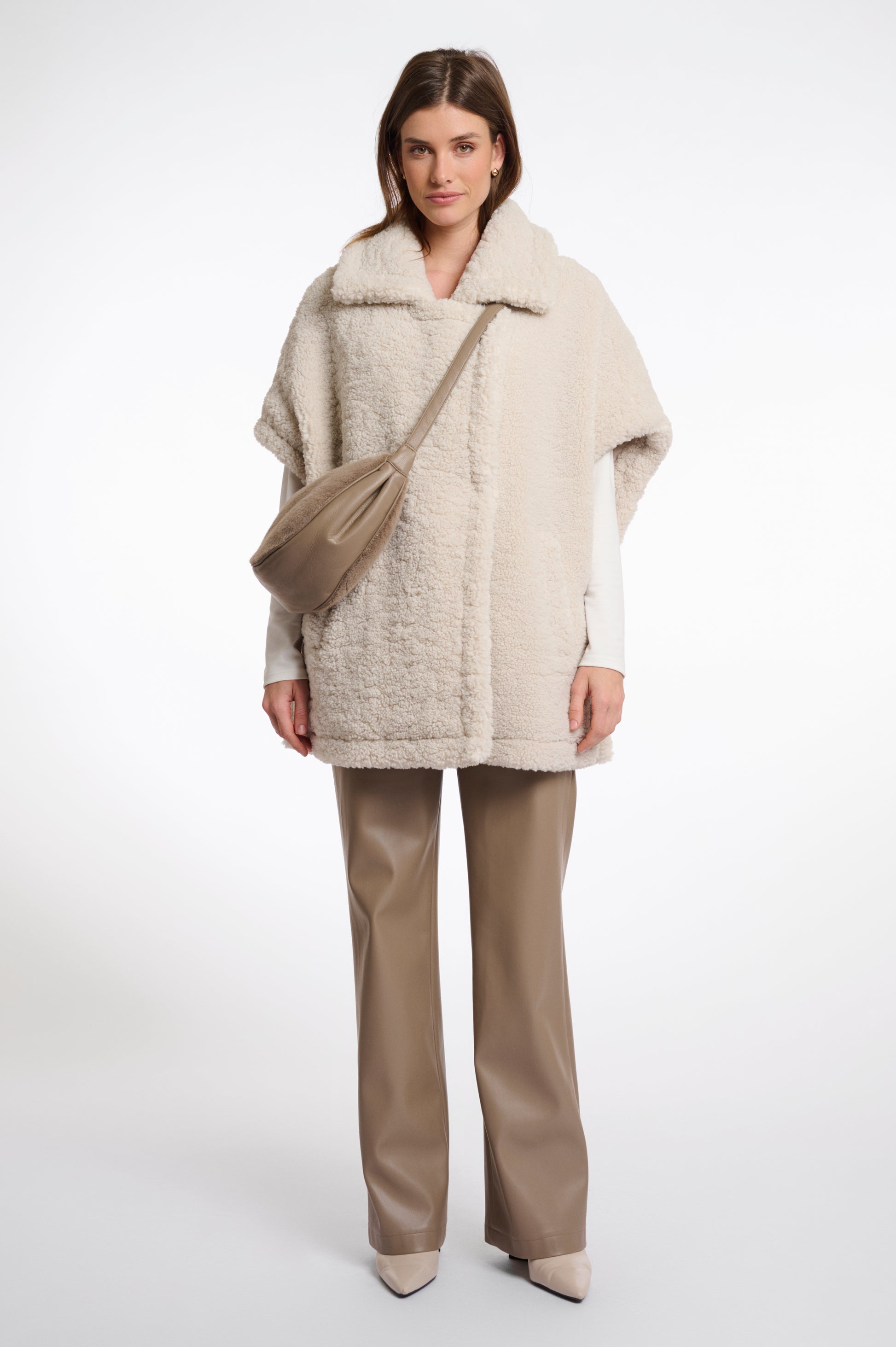 Woman wearing a beige coat and pants with a beige bag on a white background
