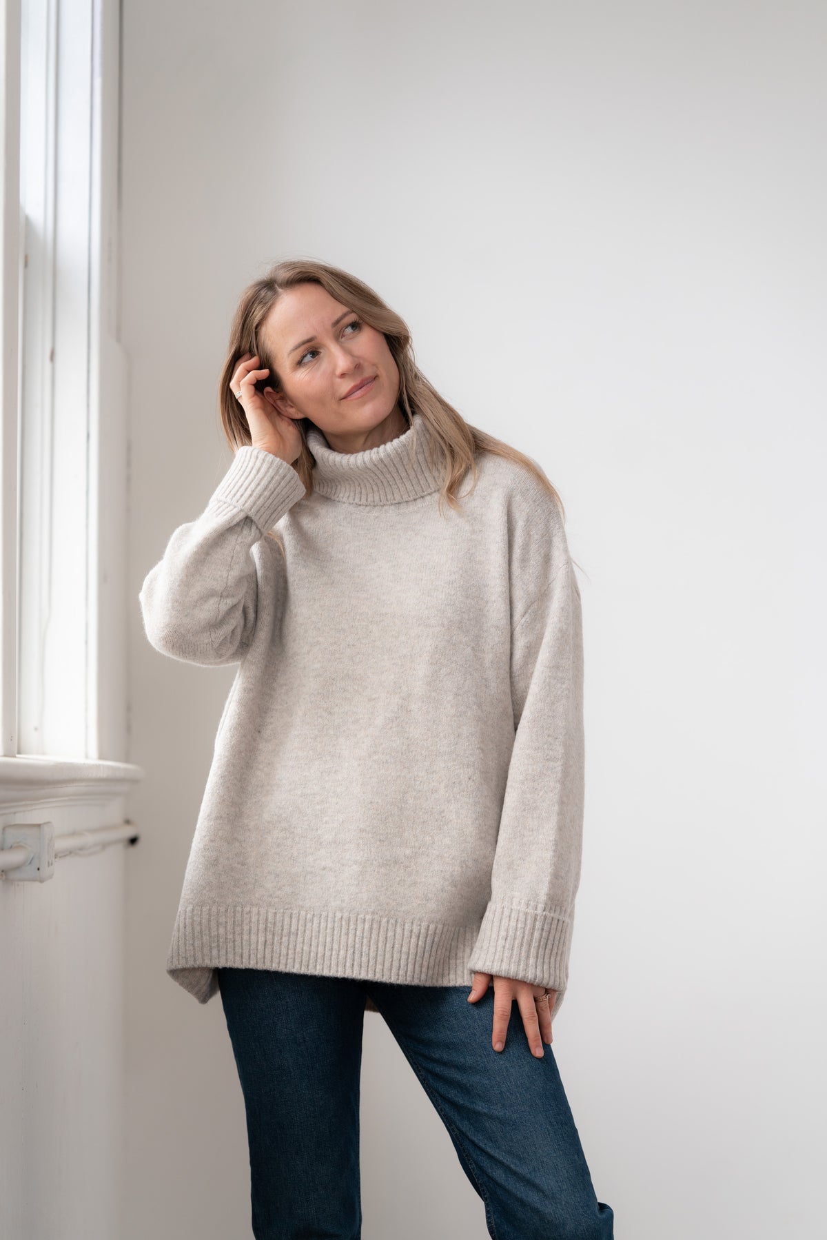 Woman wearing the Echoverde Dog Walker fawn chunky cowl neck sweater with dark jeans