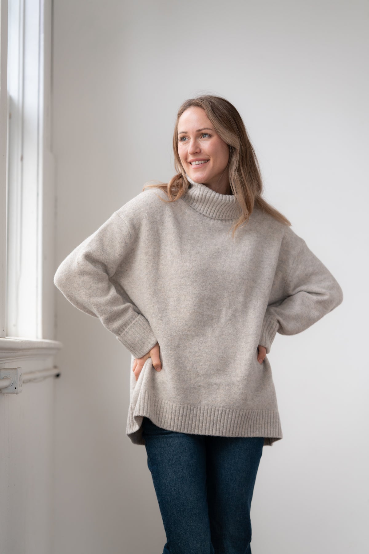 Woman wearing the Echoverde Dog Walker fawn chunky cowl neck sweater with dark jeans