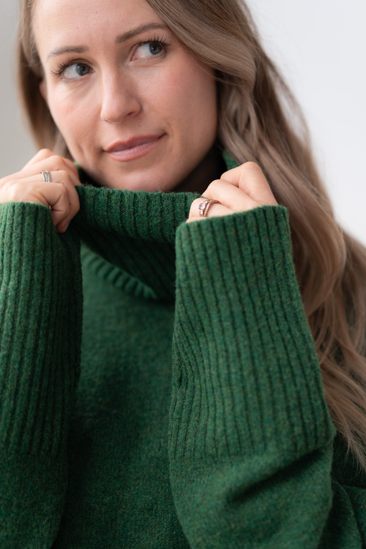 Woman wearing the Echoverde Dog Walker forest green chunky cowl neck sweater with dark jeans, pulling the cowl up over her chin