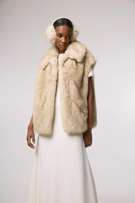 Woman wearing a cream fur vest with a plain background