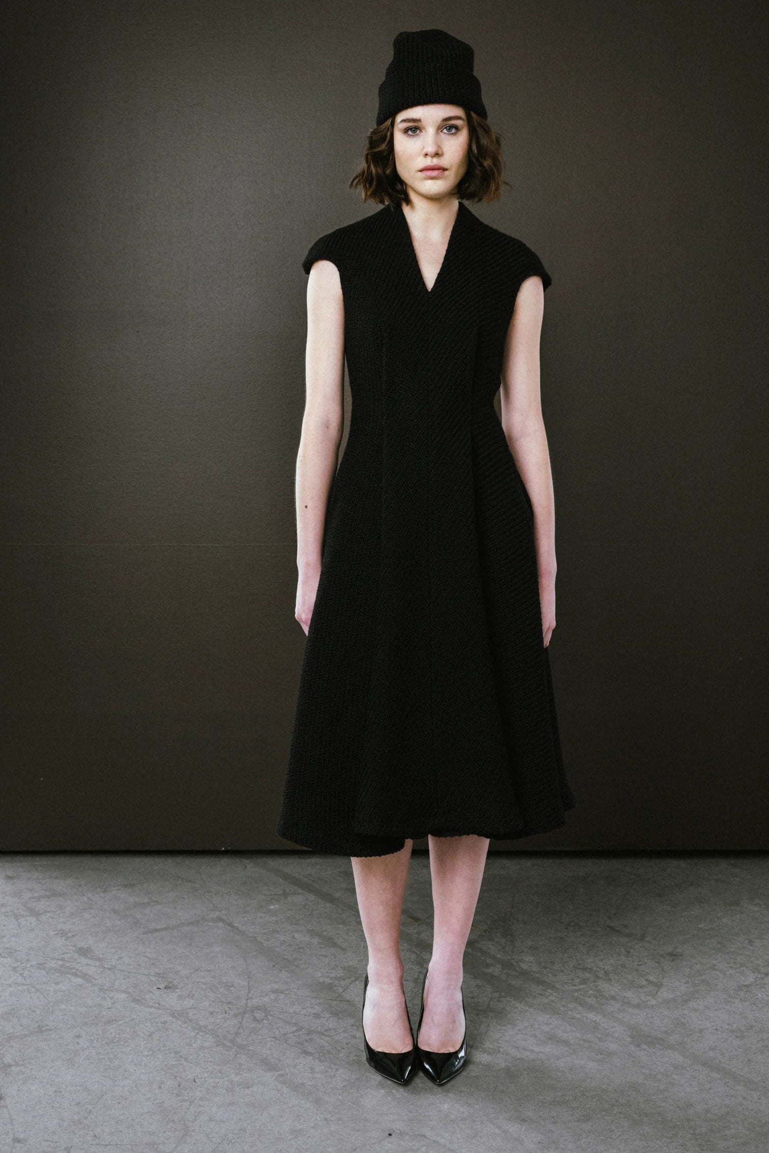 Woman wearing a black sleeveless dress and hat against a dark background