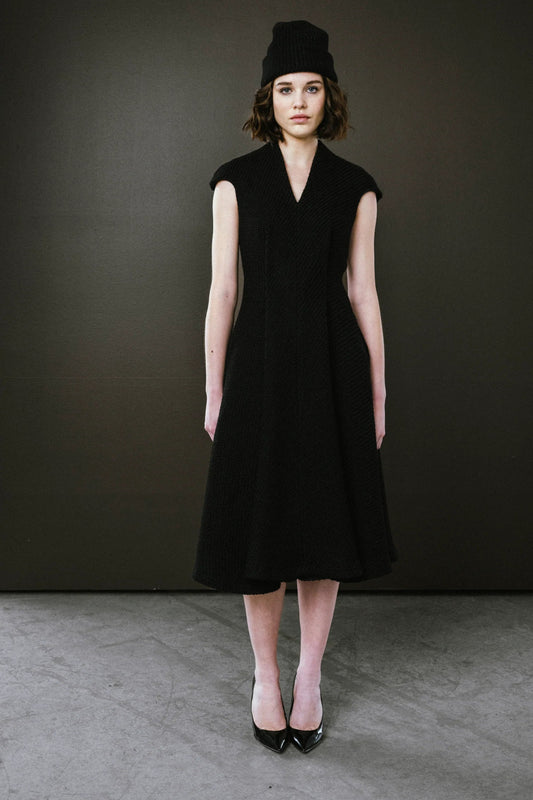 Woman wearing a black sleeveless dress and hat against a dark background