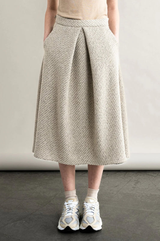 Person wearing a beige textured skirt with white sneakers on a neutral background