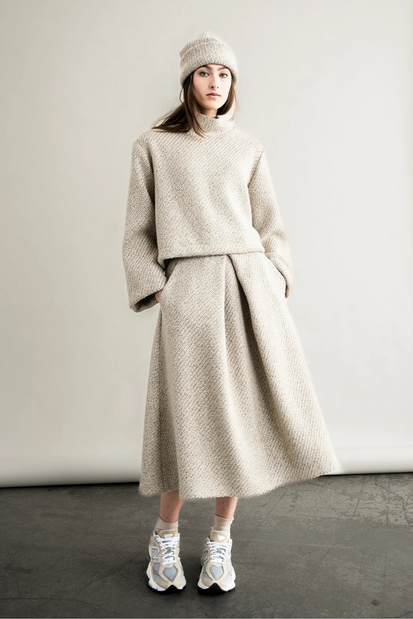 Person wearing a beige knit outfit with a skirt in a studio setting