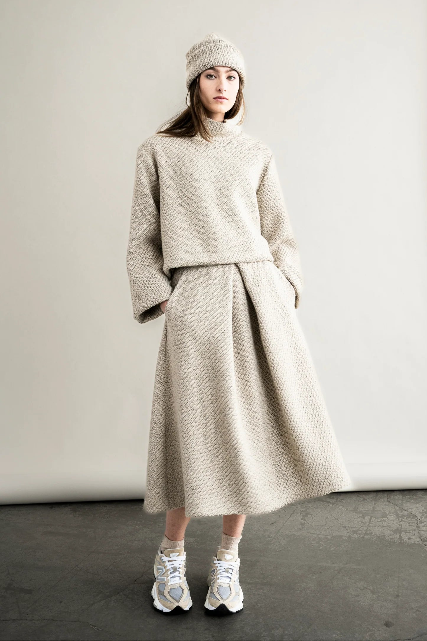 Person wearing a beige knit outfit with a skirt in a studio setting
