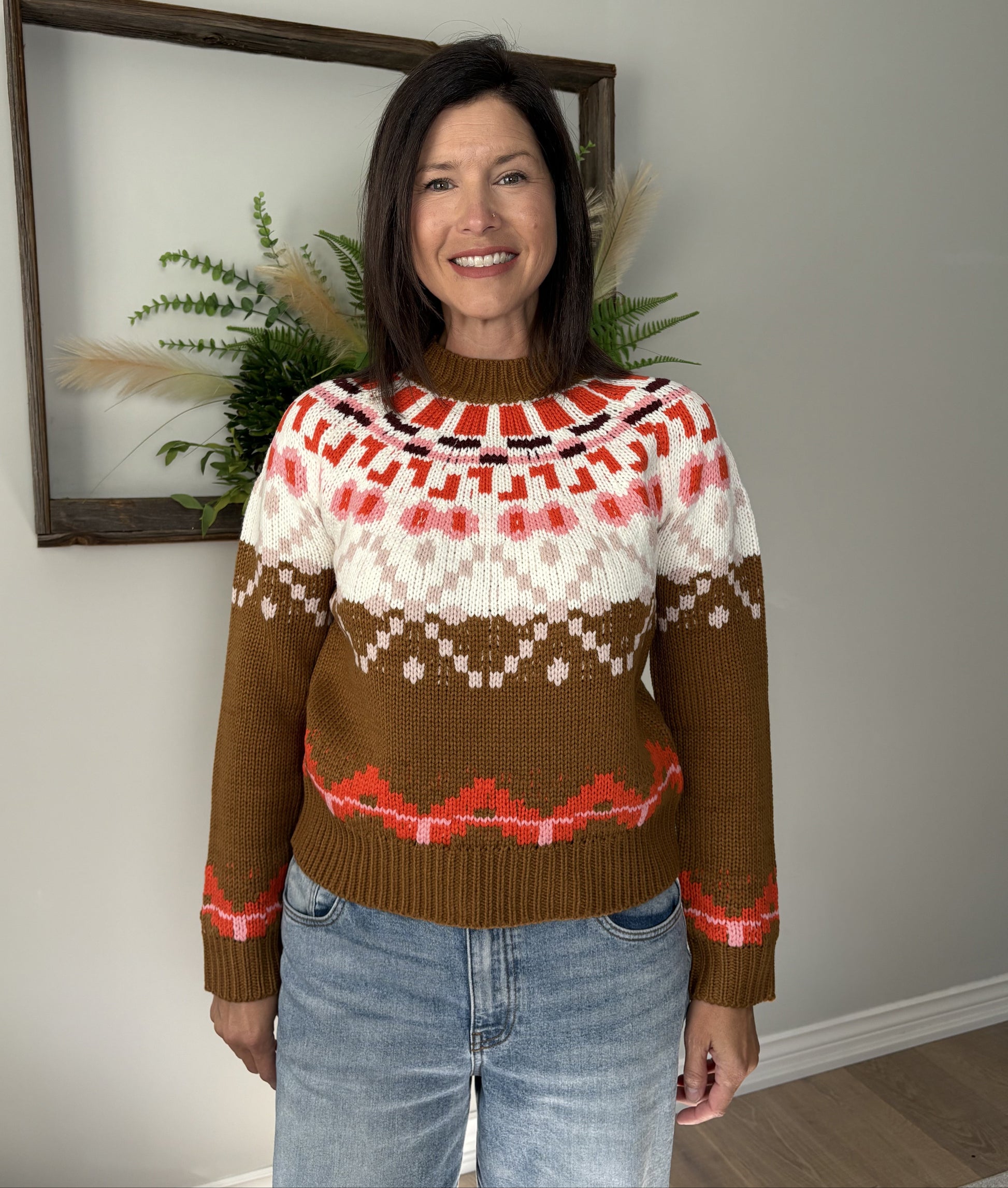 Woman wearing a patterned sweater standing indoors with a neutral background
