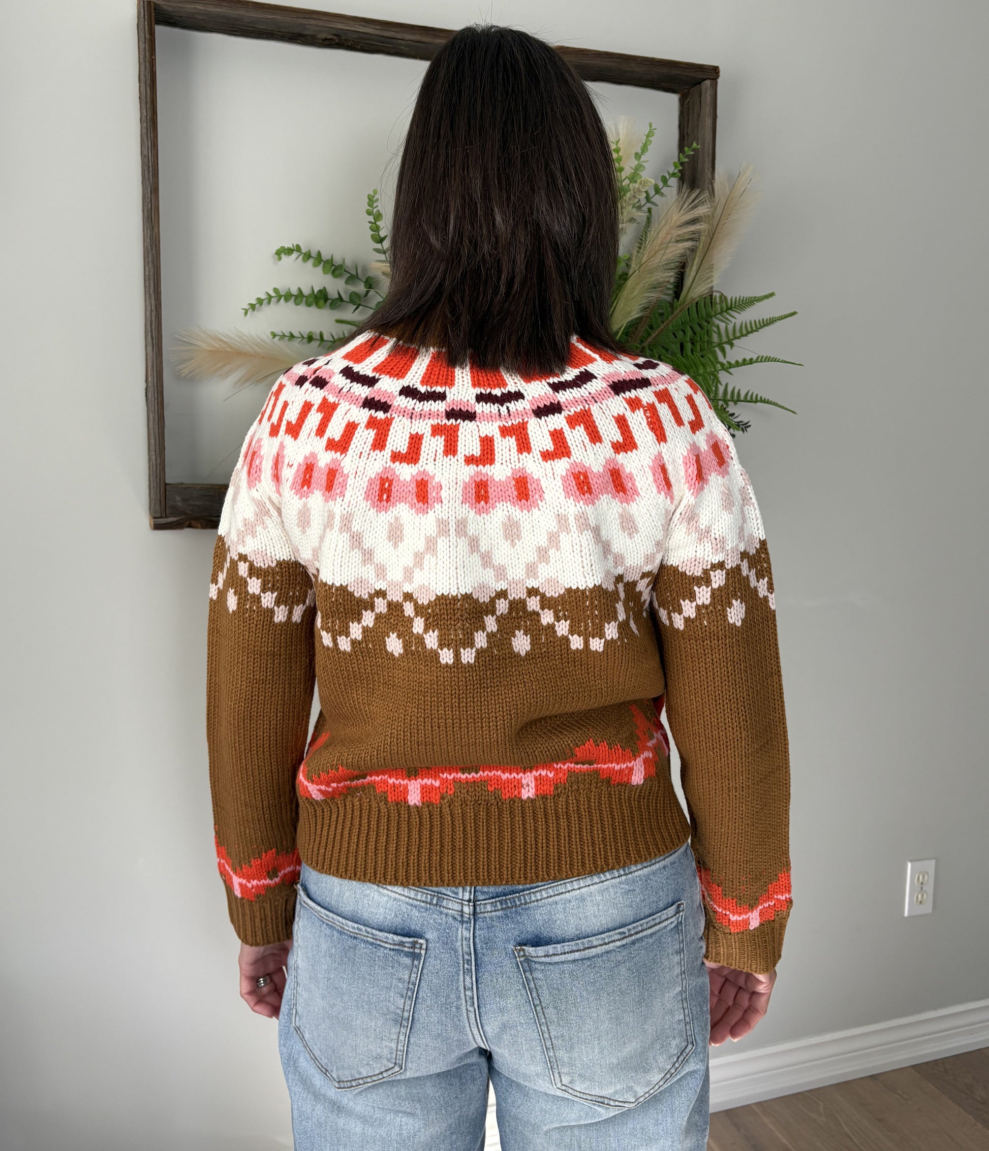 Person wearing a patterned sweater standing in front of a framed picture on a wall.