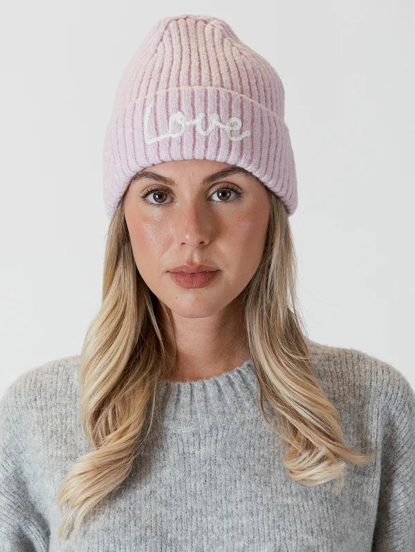 This cozy pastel pink beanie by Lyla &amp; Luxe is adorned with intricate embroidery, featuring the word "love" stitched into the soft and warm ribbed knit fabric. lemon cyprus boutique