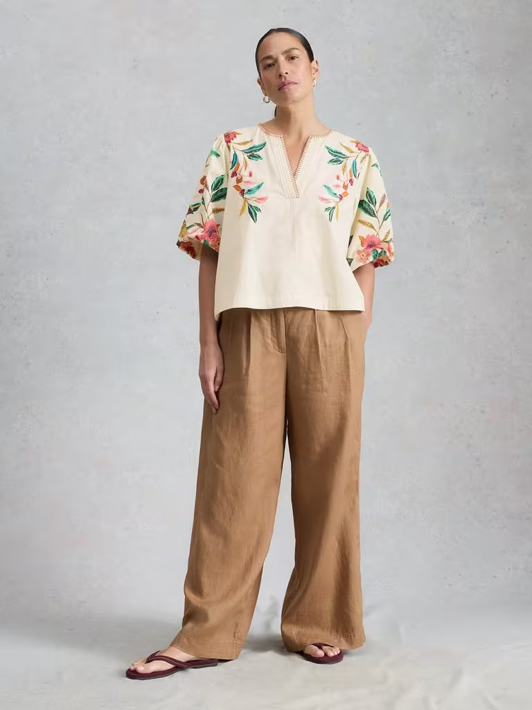 Woman wearing a floral top and beige pants on a gray background
