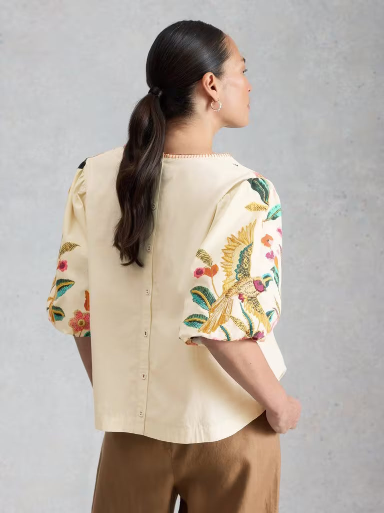 Woman wearing a beige blouse with floral embroidery on a gray background