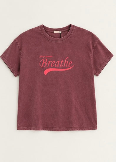 A short-sleeve crewneck t-shirt in a washed, faded burgundy color, featuring a pink graphic on the front that reads 'Always Breathe' with 'Breathe' in a larger script font and a curved underline.