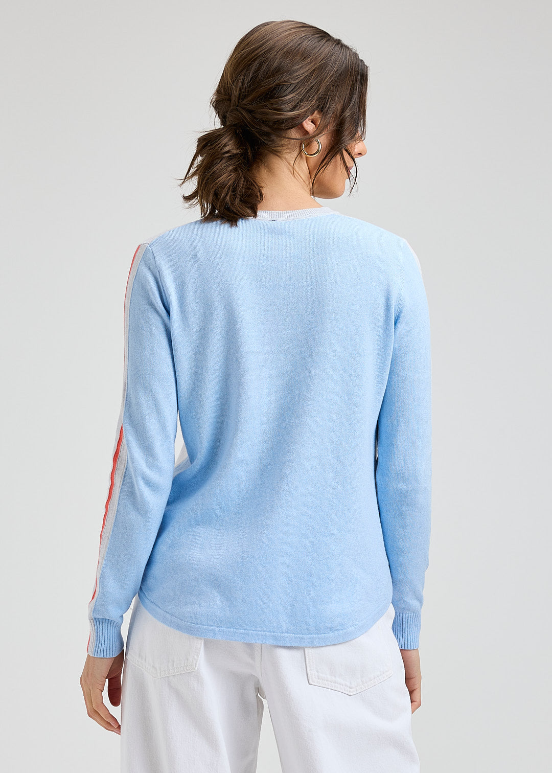Woman wearing a light blue sweater with colorful sleeves on a plain background