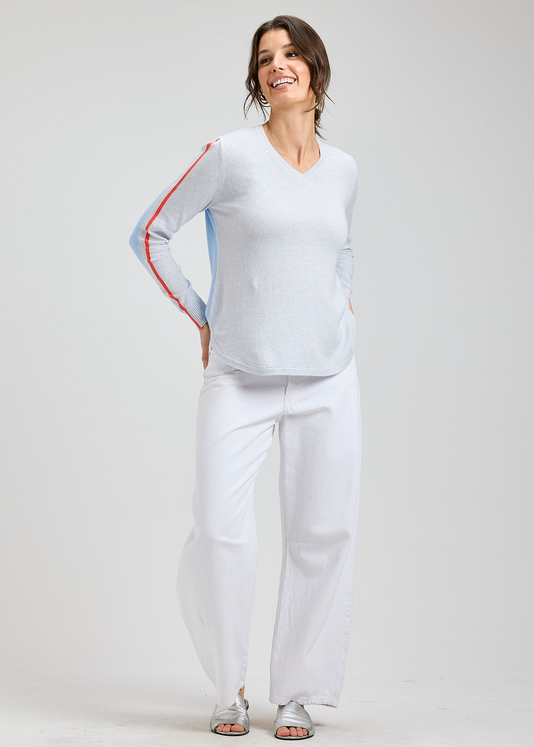 Woman wearing a light blue long-sleeve top with red accents and white pants on a plain background