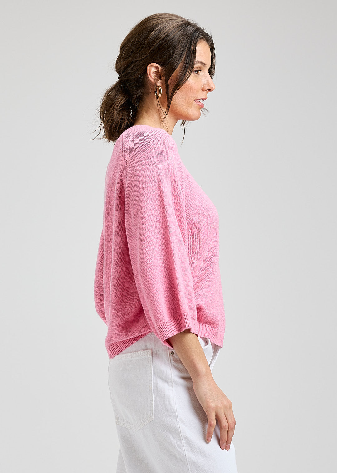 Woman wearing a pink sweater and white pants on a gray background