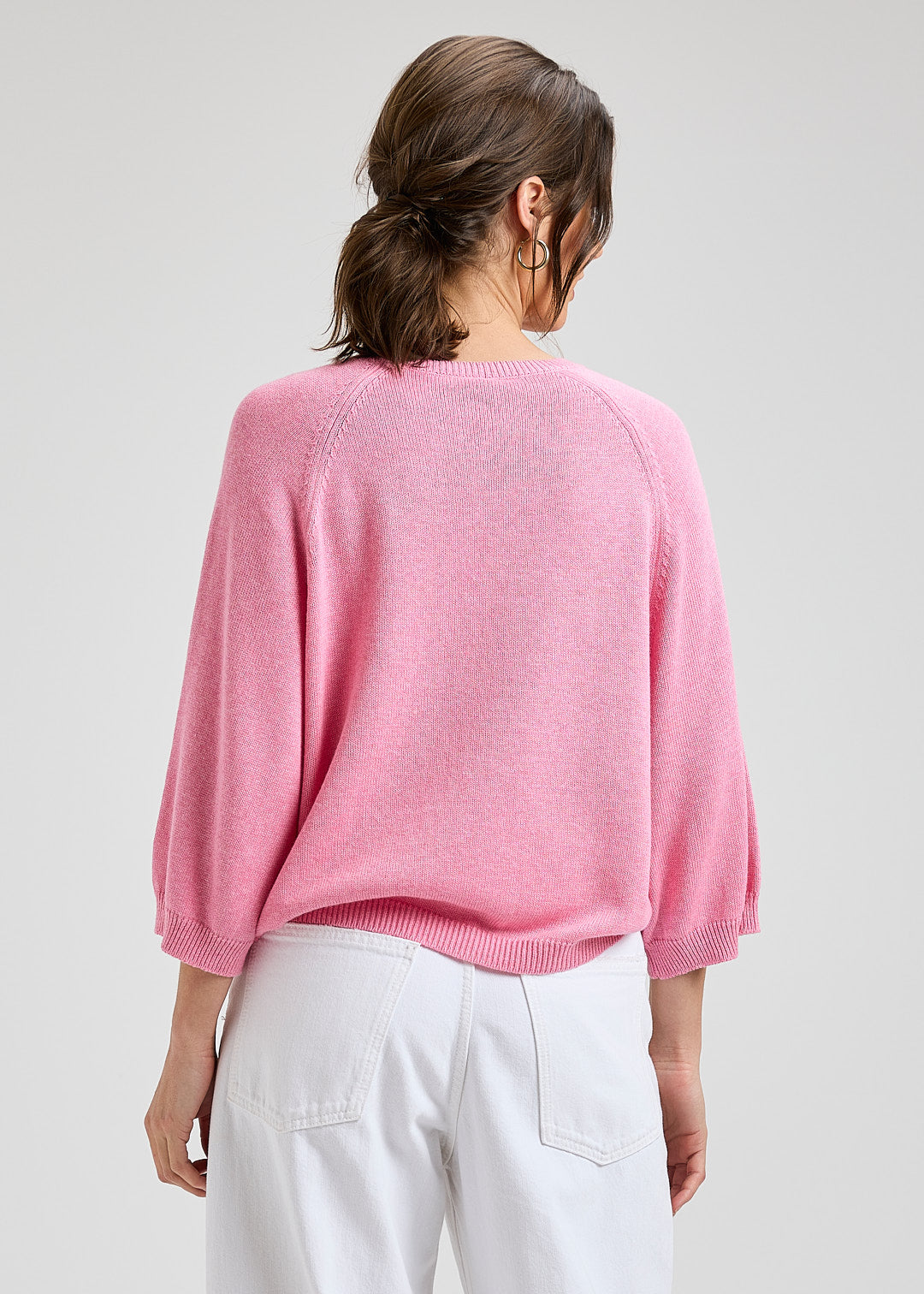 Person wearing a pink sweater and white pants on a plain background