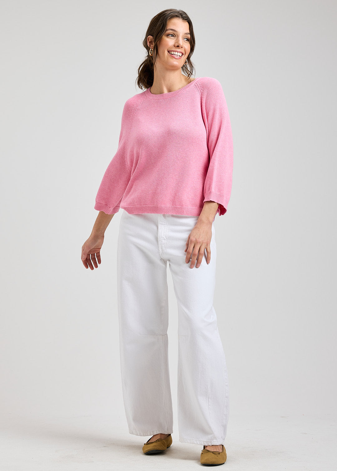 Woman wearing a pink sweater and white pants on a plain background