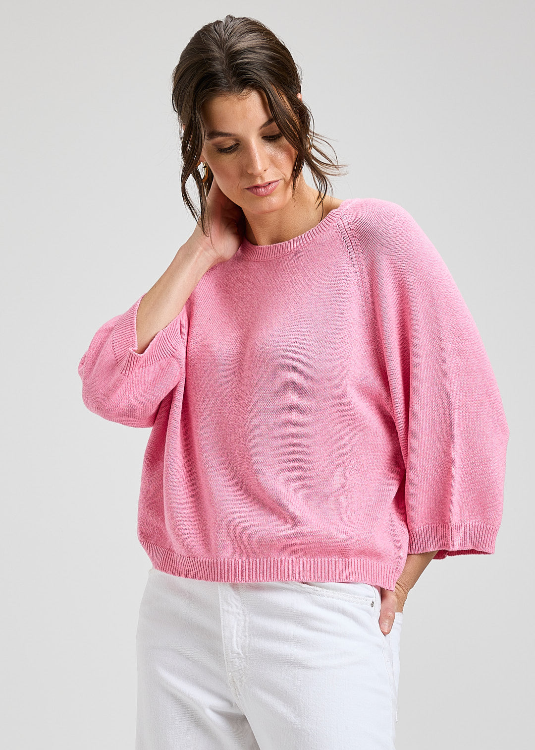 Woman wearing a pink sweater and white pants on a light gray background