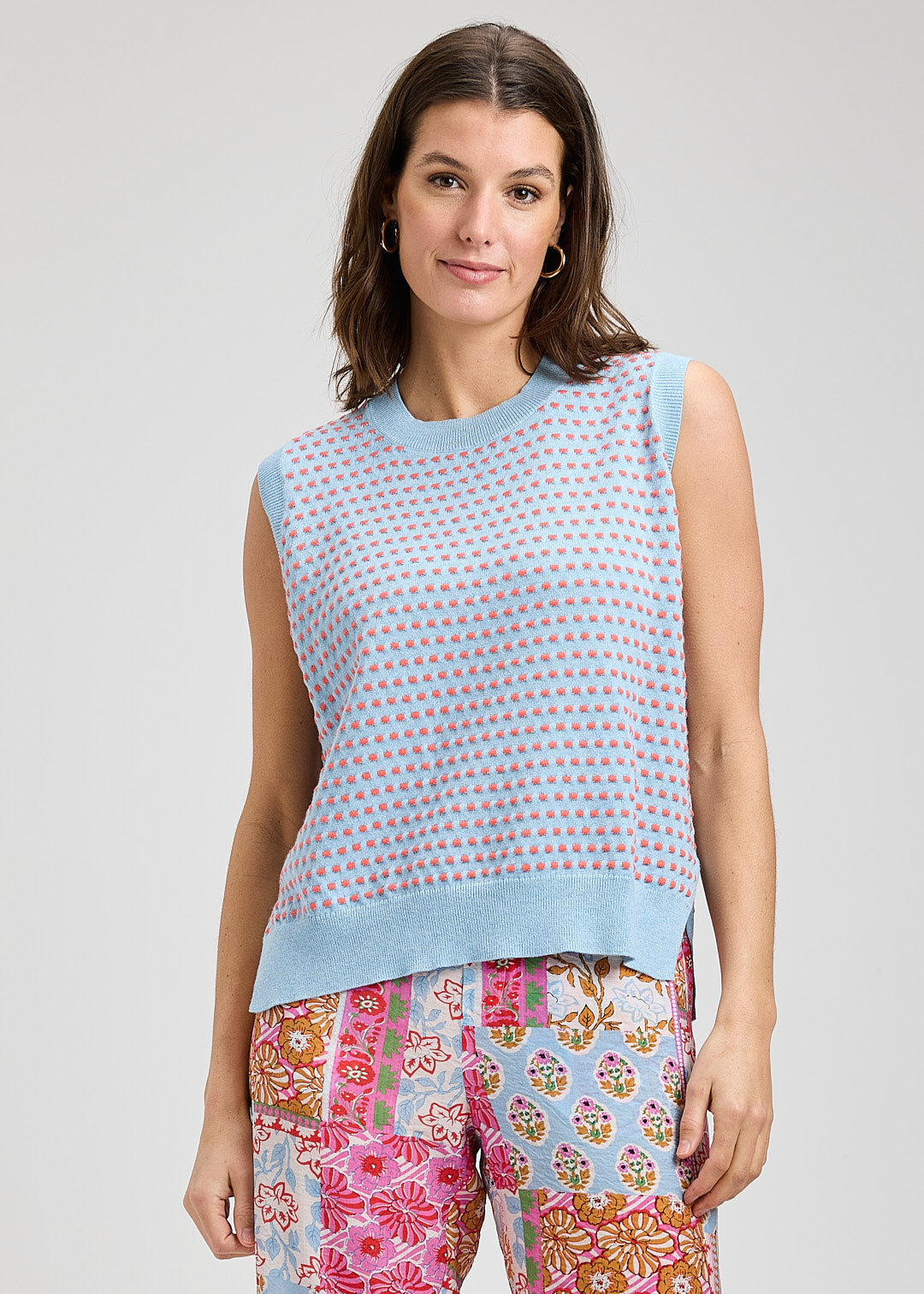 Woman wearing a sleeveless patterned top and colorful pants on a plain background