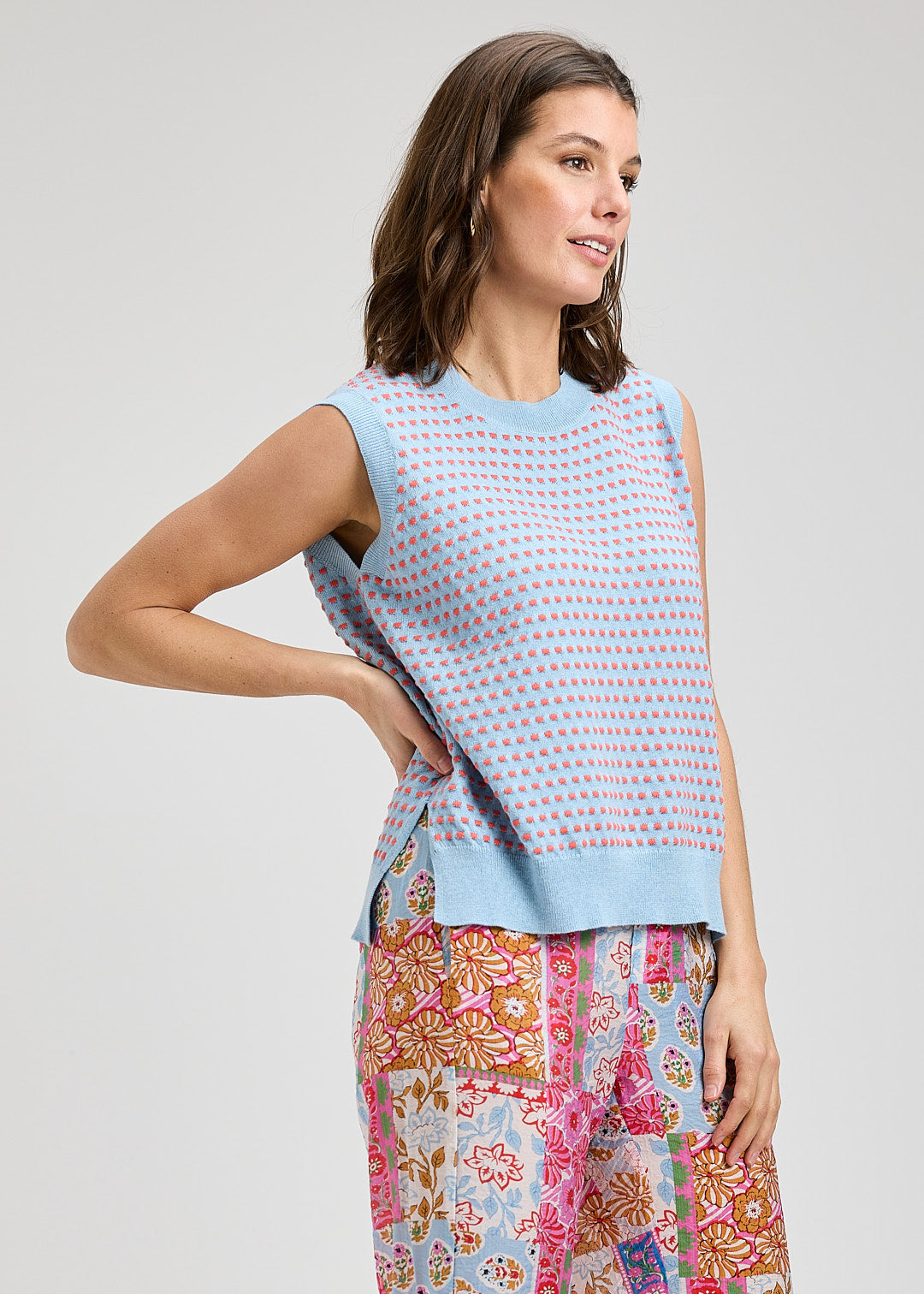 Woman wearing a sleeveless patterned top and floral pants on a plain background