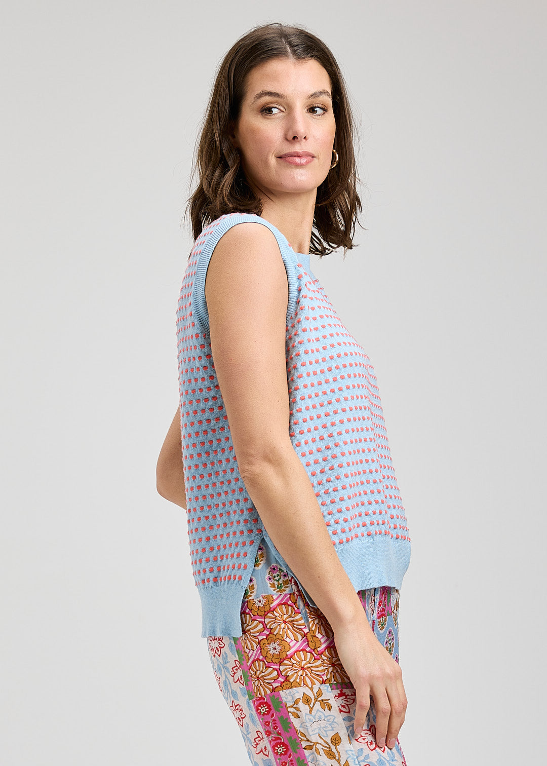 Woman wearing a sleeveless patterned top and colorful pants on a light gray background