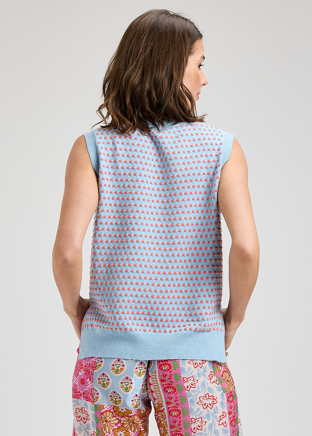 Woman wearing a sleeveless patterned top and colorful pants on a plain background