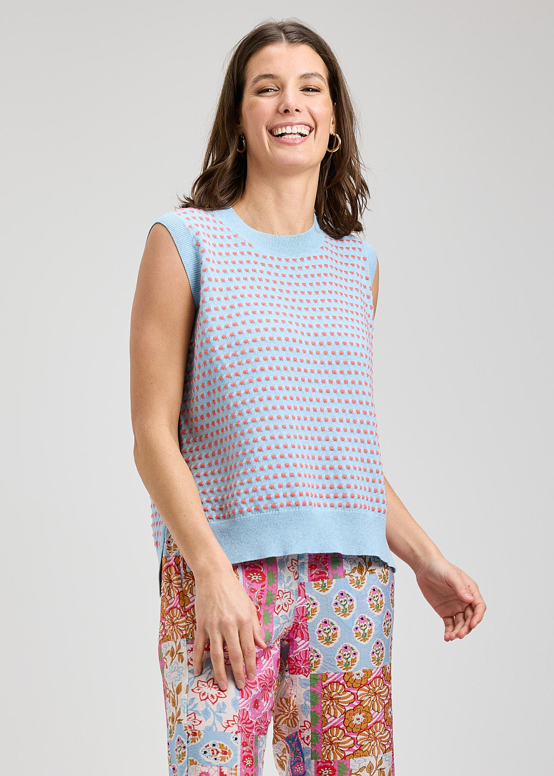 Woman wearing a sleeveless patterned top and colorful pants on a light gray background