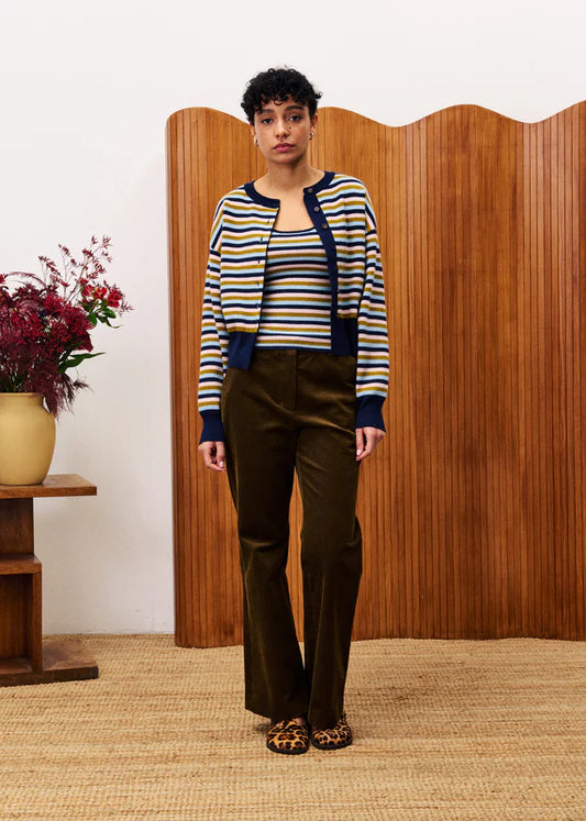 Person wearing a striped sweater and brown pants standing in front of a wooden screen.