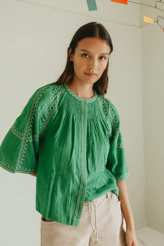 Woman wearing a green blouse with intricate patterns in a minimal indoor setting