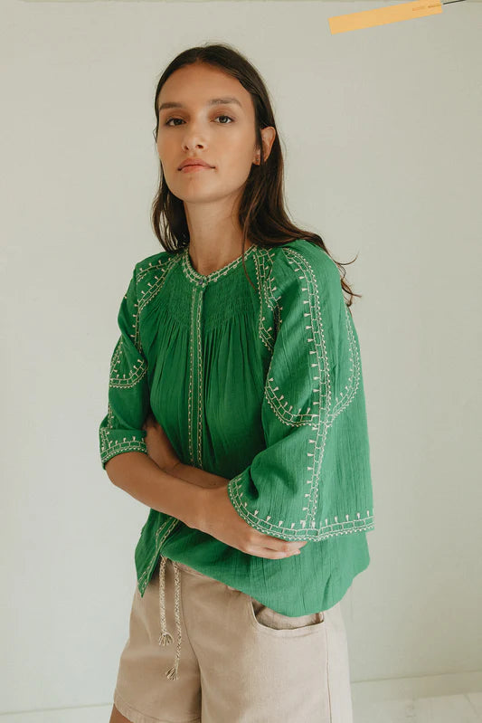 Woman wearing a green embroidered blouse against a plain background