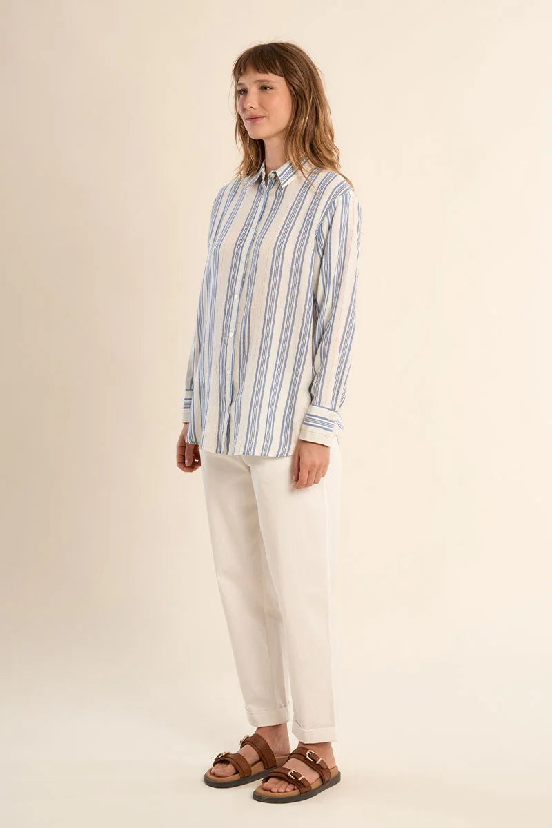 Woman wearing a blue and white striped shirt and white pants on a beige background