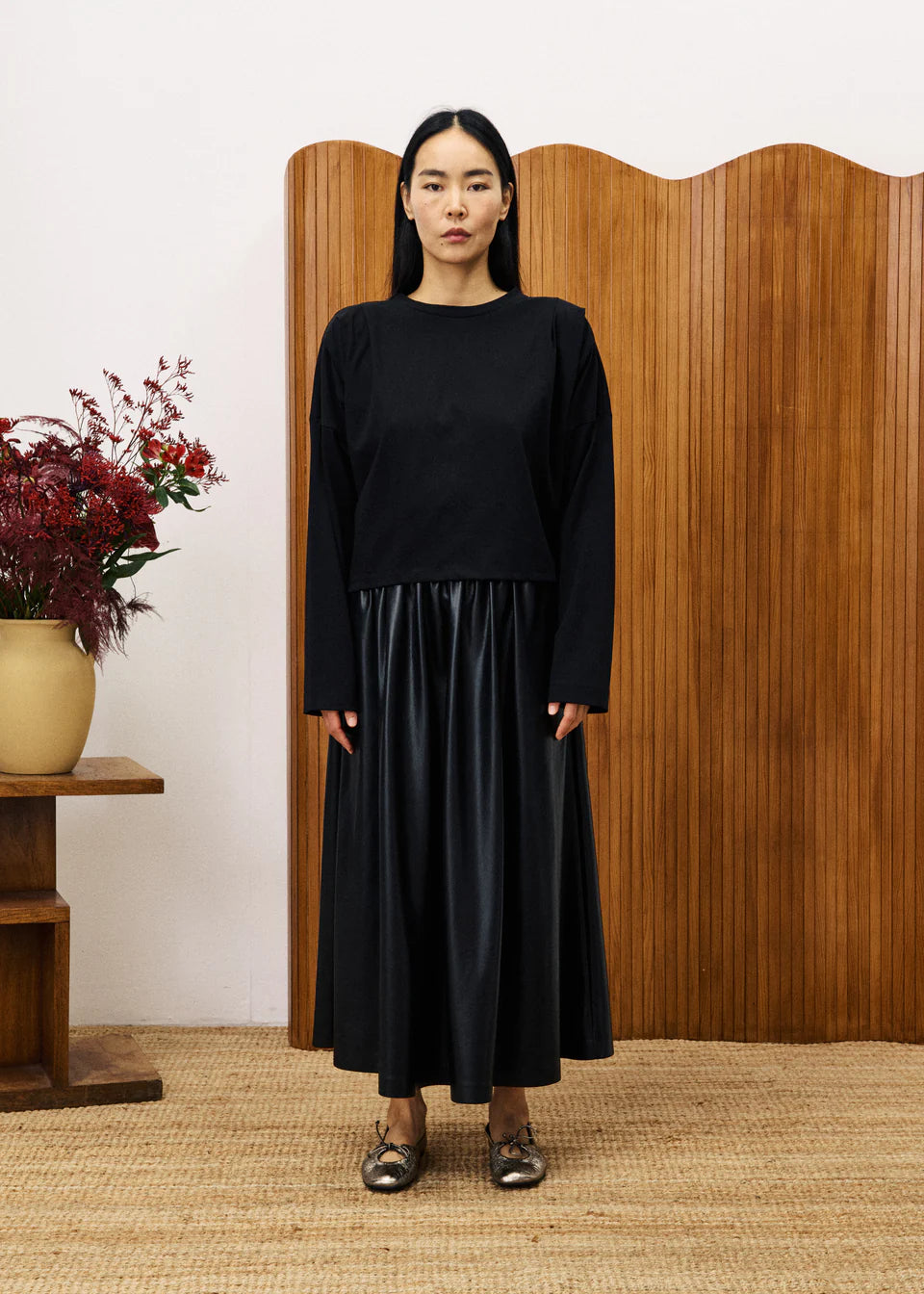 Woman wearing a black outfit standing in front of a wooden screen with floral decorations.