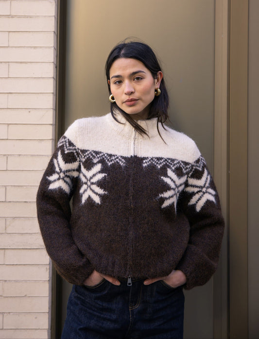 Person wearing a patterned sweater standing against a neutral wall.