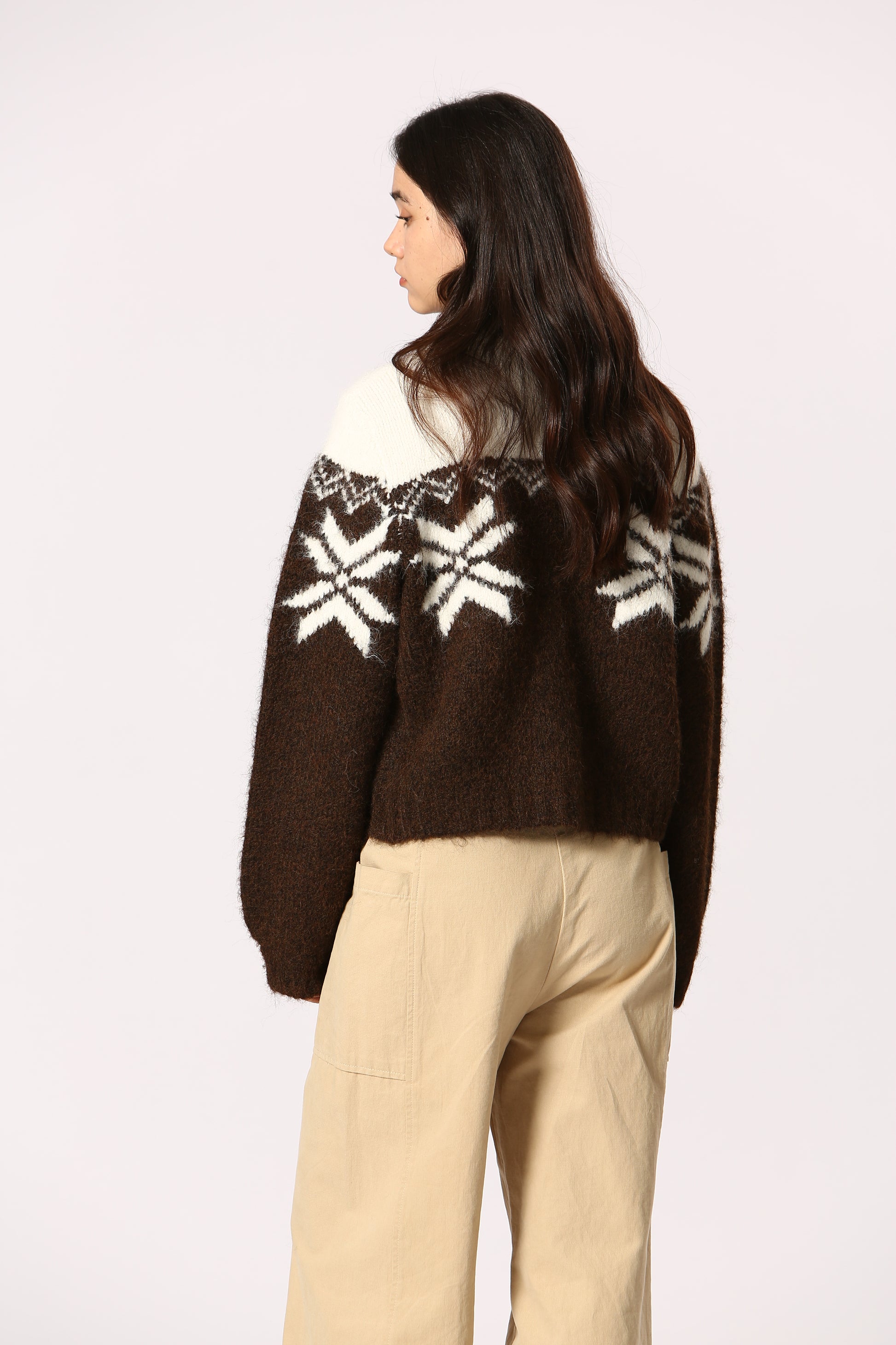 Brown sweater with white snowflake patterns worn by a person on a light gray background