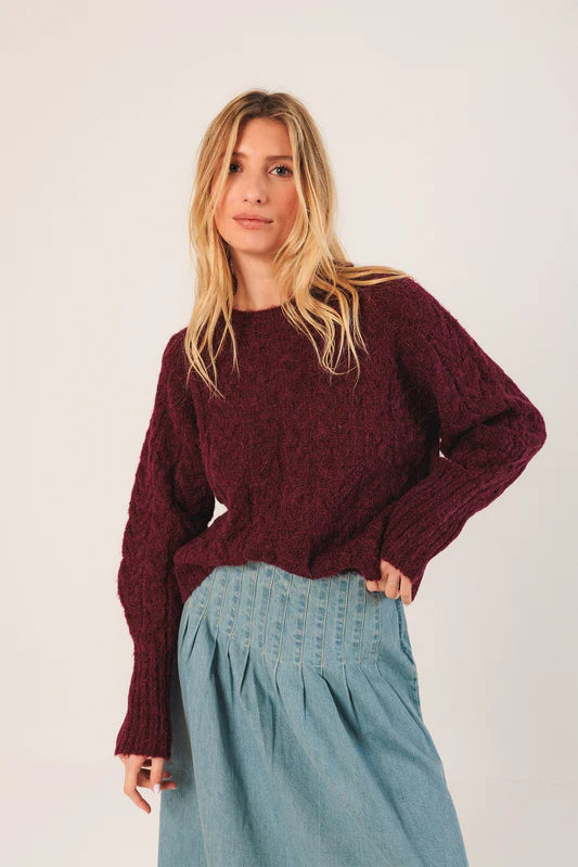 Woman wearing a burgundy sweater and light blue pants against a white background