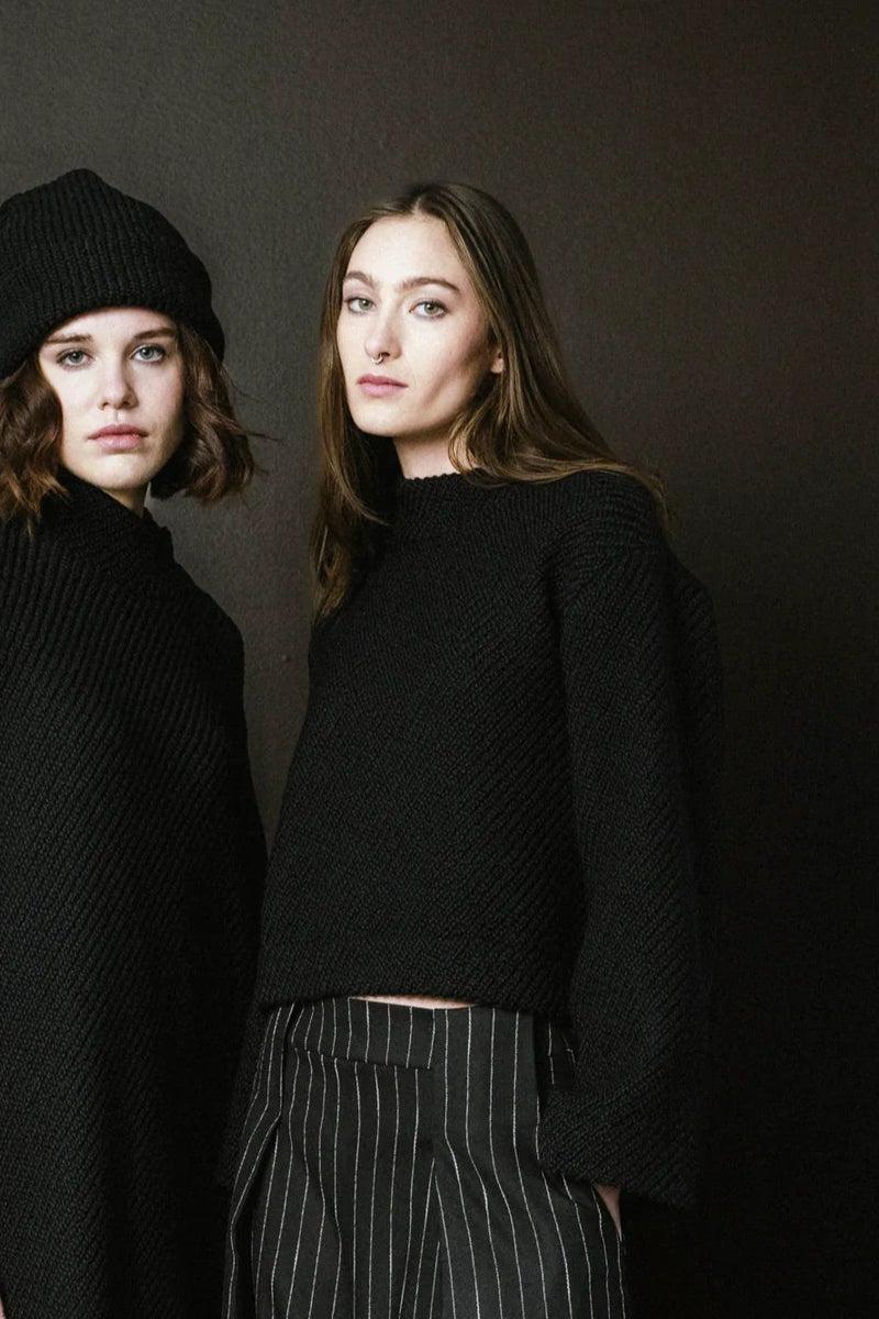 Two women wearing black outfits against a dark background