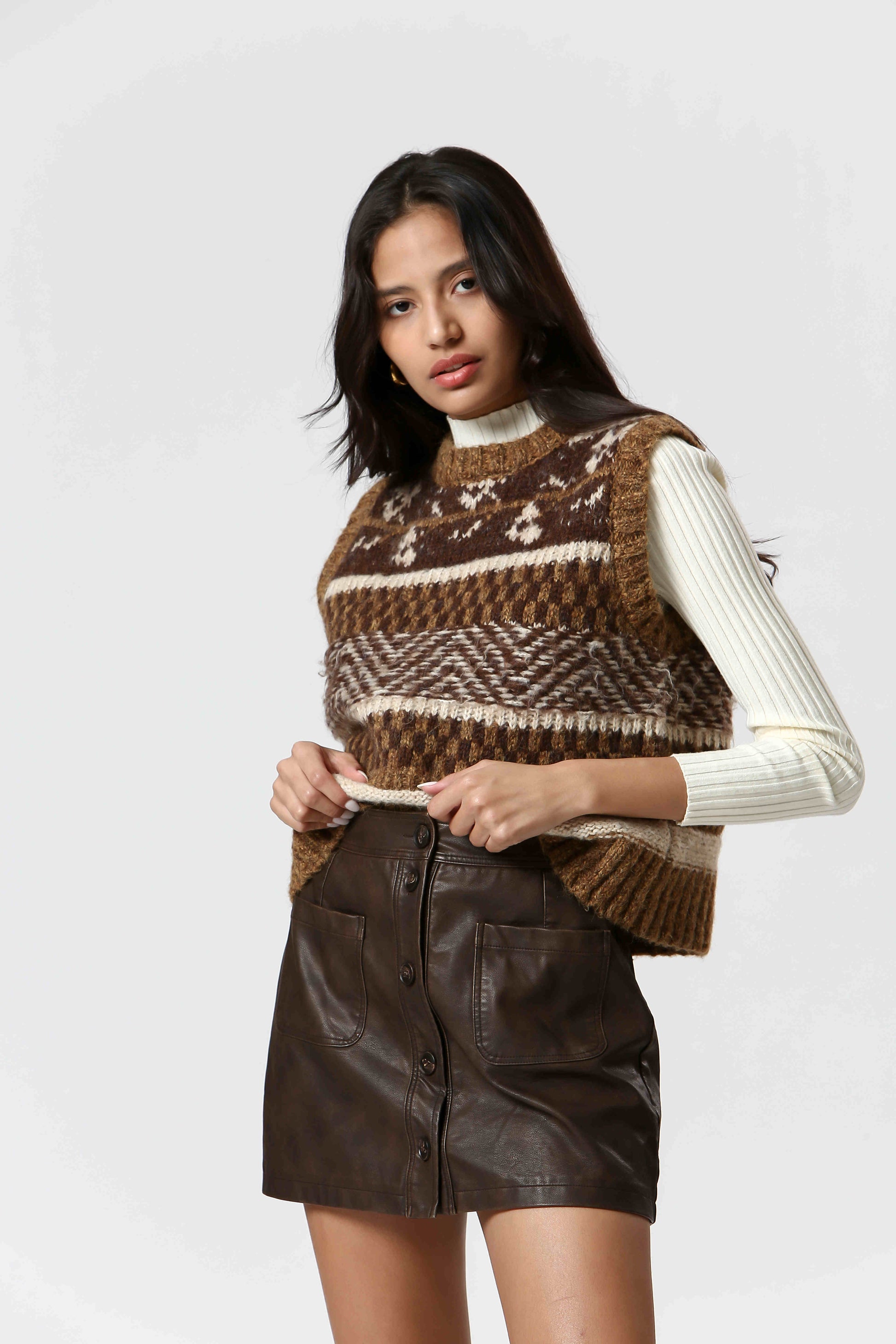 Stay cozy and stylish with The Korner's Check Sweater Vest! In shades of brown and cream, this vest features a playful check pattern with stripes, chevrons, and fairisle designs. 