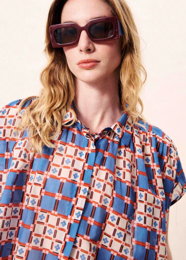 Woman wearing a patterned shirt and sunglasses against a plain background