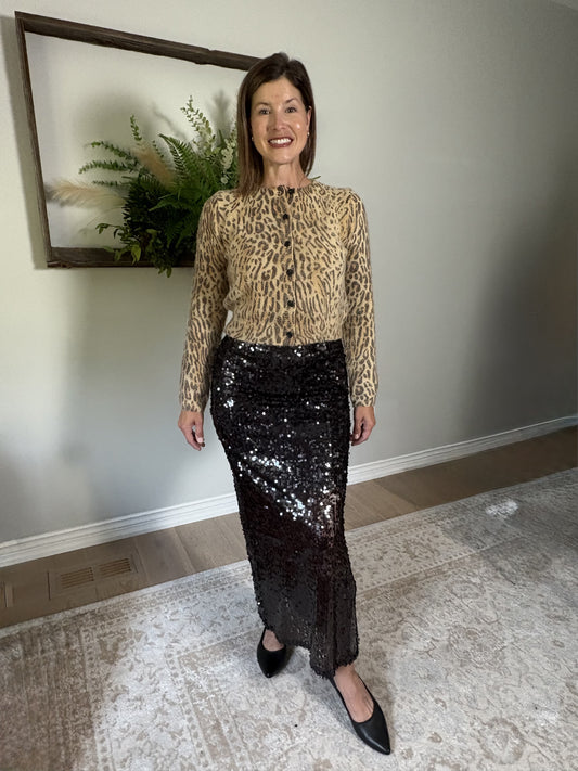 Woman wearing a leopard print top and brown sequin skirt indoors.