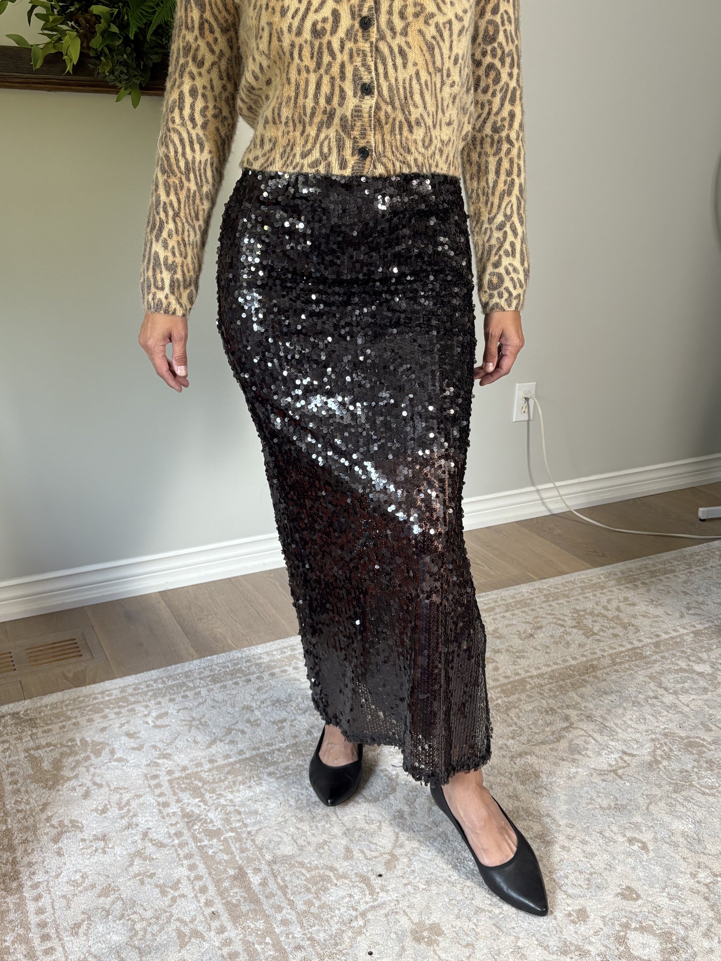 Person wearing a leopard print top and brown sequin skirt indoors.