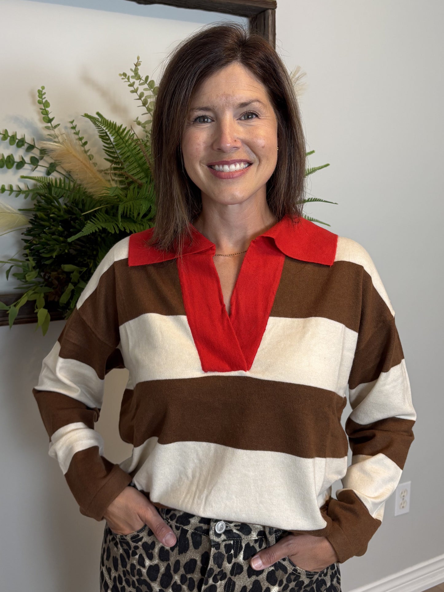 Woman wearing a striped sweater with a red collar and leopard print pants indoors.