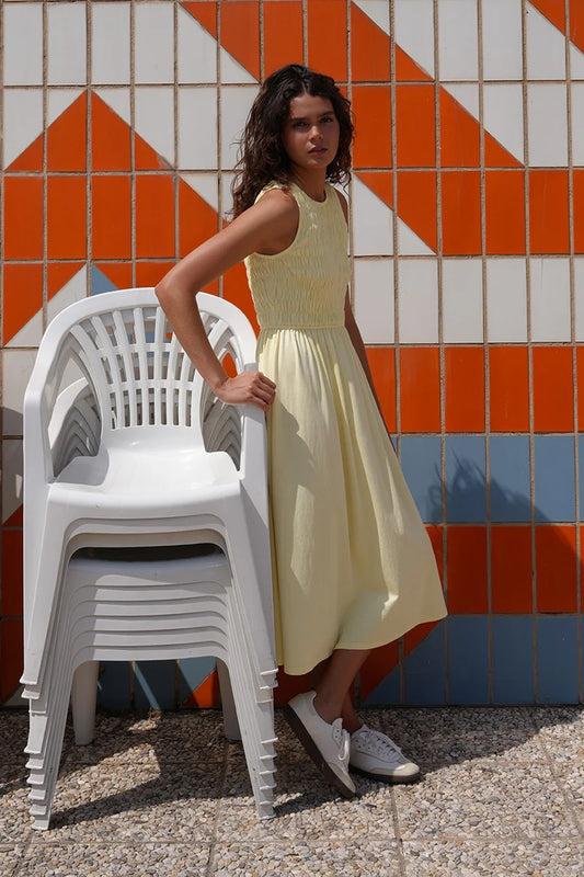 Woman in a yellow dress standing next to white chairs against a colorful tiled wall.