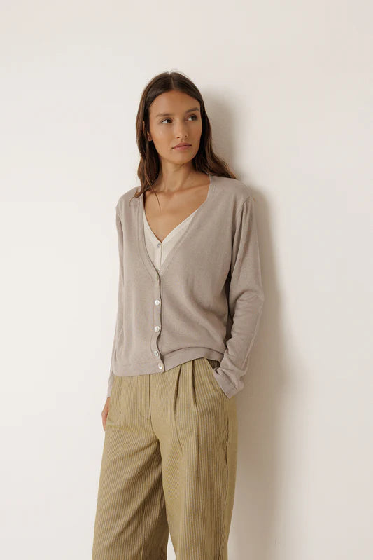 Woman wearing a light gray cardigan over a white top and beige pants against a white background