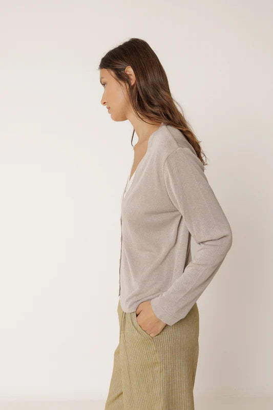 Woman wearing a light gray cardigan over a white top with beige pants against a white background