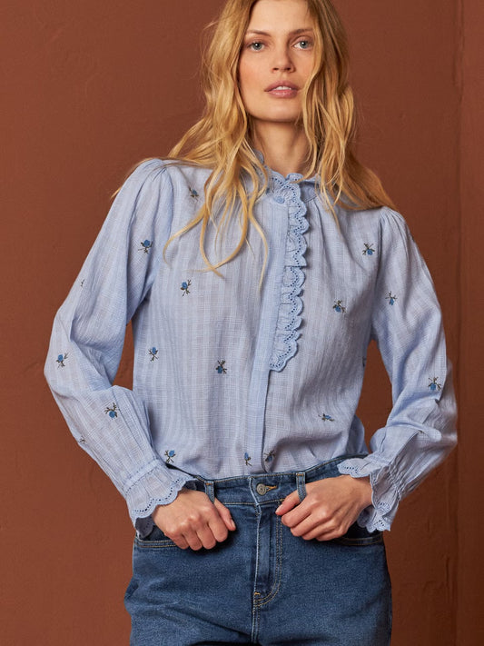 Get ready to fall in love with this embroidered shirt from Indi &amp; Cold. With a high collar, fitted shoulders, and long sleeves, this shirt is both stylish and comfortable. Made of 100% cotton gauze in a sky blue, it features beautiful embroidered floral details. The unique high collar is adorned with intricate embroidery and a ruffle finished with matching lace. The collar and cuffs are finished with delicate hemstitch details and a scalloped edge. The shirt also boasts a hidden button closure for a cle