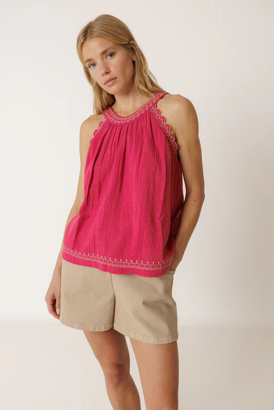 Woman wearing a pink sleeveless top with embroidery and beige shorts on a white background