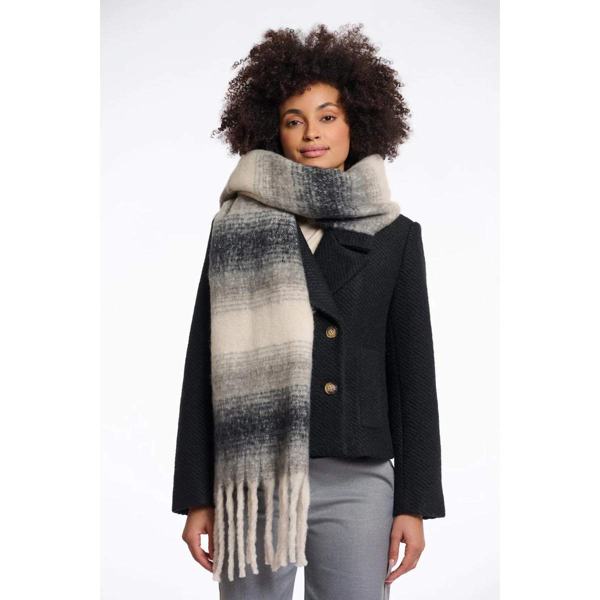 Woman wearing the Rino & Pelle Erica scarf in dark navy, light navy and cream ombré stripes with chunky fringe, styled over a dark wool jacket