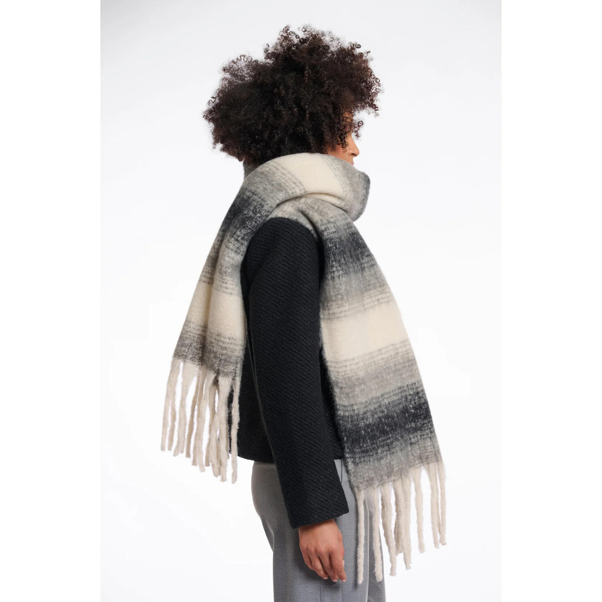 Woman wearing the Rino & Pelle Erica scarf in dark navy, light navy and cream ombré stripes with chunky fringe, styled over a dark wool jacket