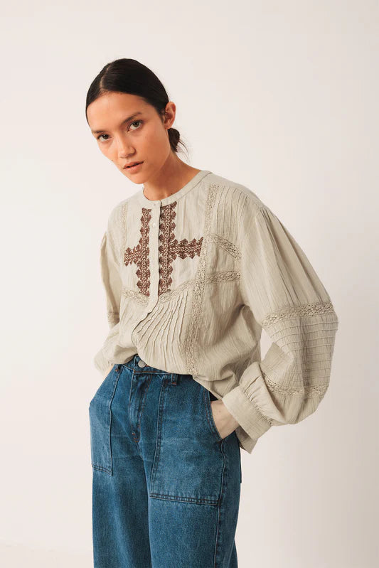Woman wearing a light-colored blouse with embroidery and blue jeans on a white background