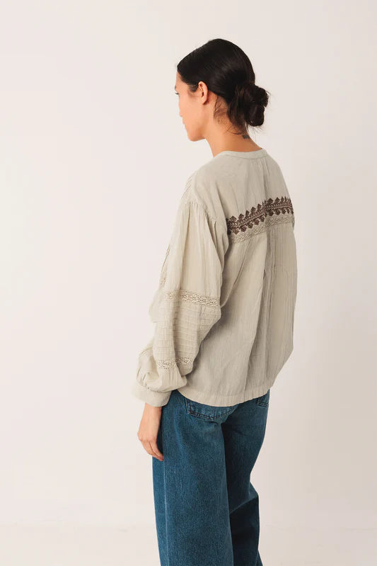 Person wearing a light green long-sleeve top with lace details on a white background